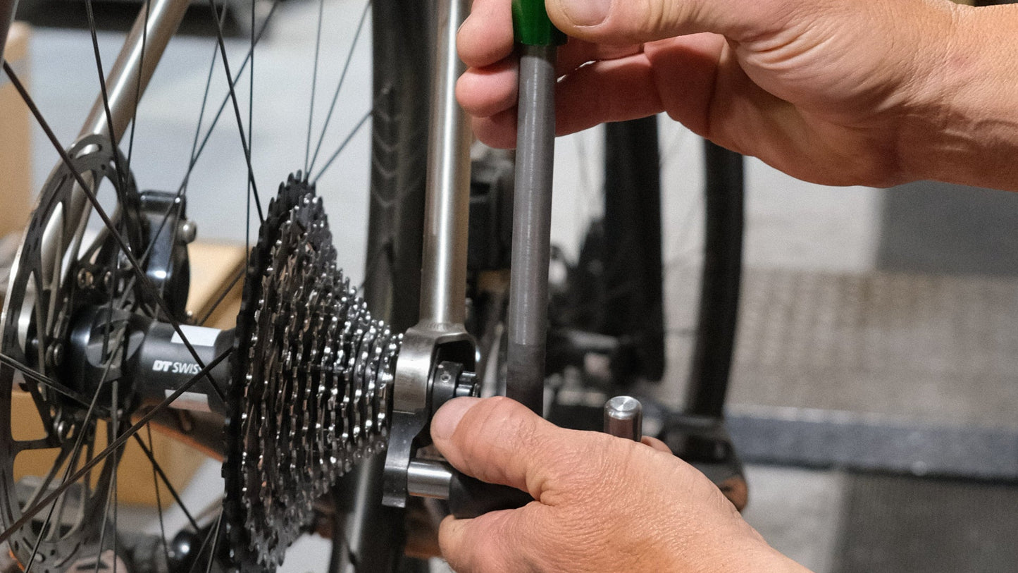 Person adjusting a bicycle wheel with a green tool in a workshop setting